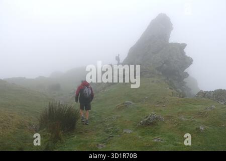 Due uomini (escursionisti) a Low Cloud sulla cima del Wainwright 'Helm Crag' (l'Howitzer) vicino a Grasmere nel Lake District National Park, Cumbria. REGNO UNITO Foto Stock