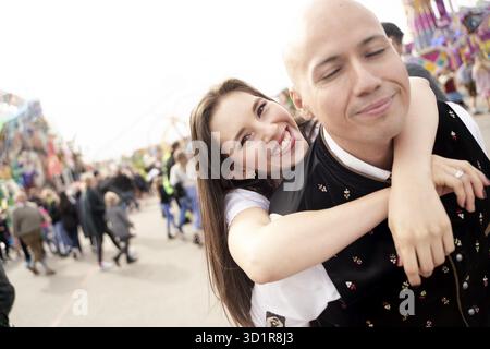 Felice fidanzata moglie appesa alle spalle del fidanzato marito al Fun Fair Oktoberfest di Monaco, Baviera, Germania, Europa, uscire insieme, dati Foto Stock