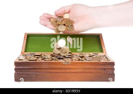 Mano la caduta delle monete in uno scrigno del tesoro Foto Stock