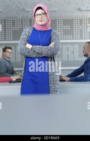 Giovane donna islamica con un gruppo di studenti vestiti con abiti tradizionali all'interno dell'ambiente scolastico Foto Stock