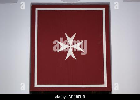 Simbolo della croce maltese presentato su uno stendardo rosso con un bordo bianco, che rappresenta concetti storici o spirituali Foto Stock