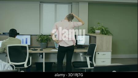 Lavoratrice d'ufficio che indossa una camicia rosa che tiene la testa nell'armadio, con monitor e piante in vaso Foto Stock