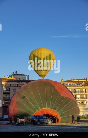 Guadix, Granada - Spagna - 01-24-2024: Una mongolfiera gialla galleggia sopra una grande mongolfiera parzialmente riempita con segmenti rossi e verdi a terra Foto Stock