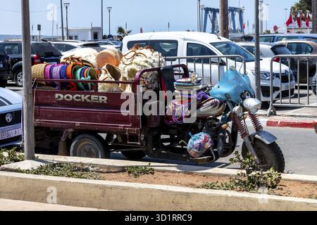 Cordoba, Cordoba - Spagna - 04-08-2024: Un veicolo Docker a tre ruote carico di cesti colorati e merci è parcheggiato accanto alle auto aziendali Docker Foto Stock