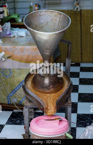 Cordoba, Cordoba - Spagna - 04-08-2024: Imbuto metallico per la produzione di olio di argan, sostanza marrone che fluisce in un contenitore di plastica Foto Stock