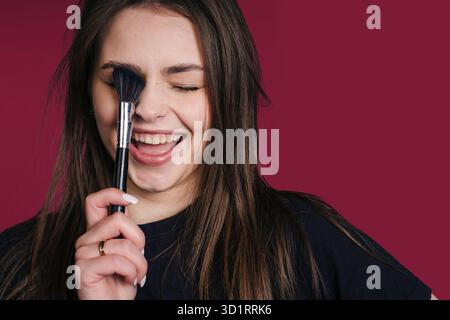 donna rilassata con spazzola, primo piano di donna sorridente con pelle impeccabile che prova i nuovi strumenti per il trucco Foto Stock