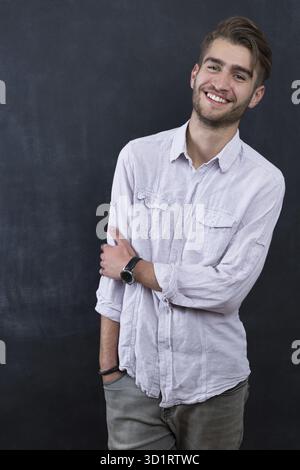 Ritratto di giovane sorridenti insegnante uomo in piedi vicino a sfondo lavagna Foto Stock