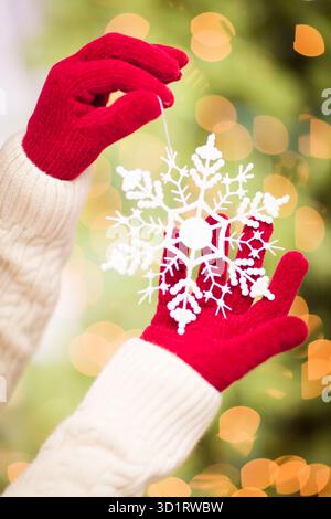 Donna che indossa i mittens rossi stagionali tenendo in mano l'ornamento natalizio bianco fiocco di neve Foto Stock