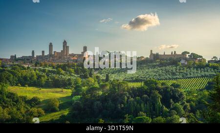 Vista panoramica della città medievale di San Gimignano con le sue famose torri che si innalzano sopra la campagna toscana circostante e i vigneti al tramonto, T Foto Stock