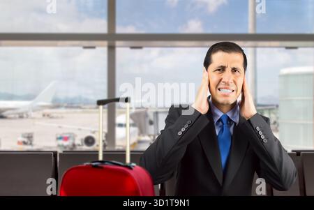 Ritratto di un uomo d'affari che si copre le orecchie con la mano per non sentire il grande rumore all'aeroporto Foto Stock