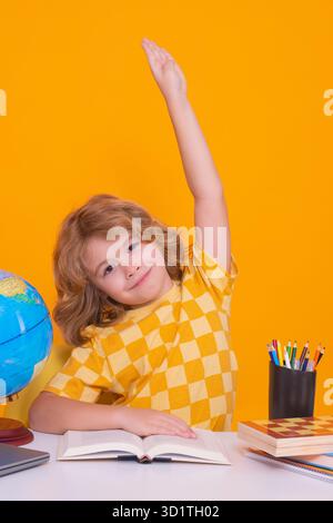 Figlio di scuola che alza la mano, pronto a rispondere alla domanda. Bambino che studia in classe alla scuola elementare. Ragazzo che studia sul giallo Foto Stock