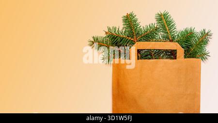 Un semplice sacchetto di carta marrone pieno di rami di pino fresco, perfetto per regali natalizi ecologici. Banner per festeggiamenti sostenibili con copia Foto Stock