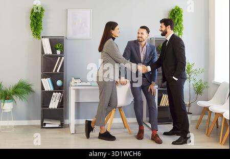 Tre partner commerciali felici che si trovano in ufficio e stringono la mano dopo aver concluso un accordo di successo. Foto Stock