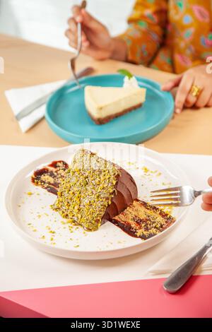 Gli amici si godono una fetta di torta al pistacchio e al formaggio lampone servita in un ristorante caffetteria. Foto Stock