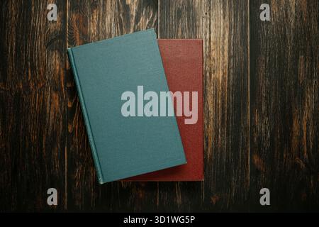 Due libri vuoti, verde acqua e Borgogna, impilati su uno sfondo di legno scuro e ricco. Foto Stock