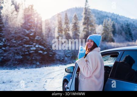 Viaggiatrice felice che ammira le montagne innevate che escono dall'auto. Autista che guarda il paesaggio invernale. Viaggiare in auto. Viaggio a Carpazi per vacanze Foto Stock