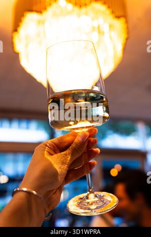 Mano che tiene il bicchiere di vino bianco sotto il candelabro Foto Stock