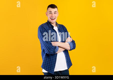 Allegro giovane uomo in piedi con le braccia incrociate davanti a uno sfondo giallo brillante Foto Stock