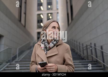 Una donna d'affari sale le scale vicino a un business center, tenendo il telefono Foto Stock