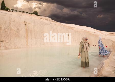 Donne che indossano l'hijab Wading nelle piscine termali di Pamukkale, Türkiye (Turchia), sotto nuvole di tempesta buie al tramonto. Foto Stock