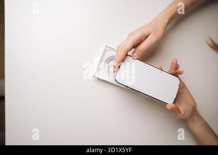 Primo piano di mani femminili che aprono un moderno smartphone, rivelando un dispositivo elegante su un tavolo bianco minimalista, mostrando un'anticipazione durante la fase iniziale Foto Stock