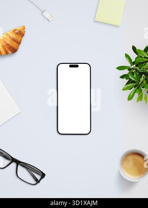 Vista dall'alto dello smartphone con schermo bianco vuoto, caffè, croissant e bicchieri sulla scrivania luminosa, che rappresenta il concetto di spazio di lavoro digitale pulito Foto Stock