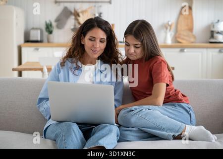 La famiglia moderna madre e figlia guardano film online guardando lo schermo del notebook mentre si riposano a casa Foto Stock