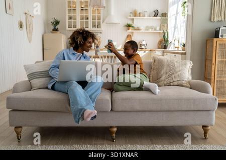 Buon famiglia afro-americana madre e figlio godere fine settimana a casa riposo sul divano con gadget Foto Stock