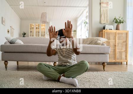 Piccolo ragazzo afro-americano curioso che indossa occhiali per la realtà virtuale e che passa del tempo nel mondo virtuale Foto Stock