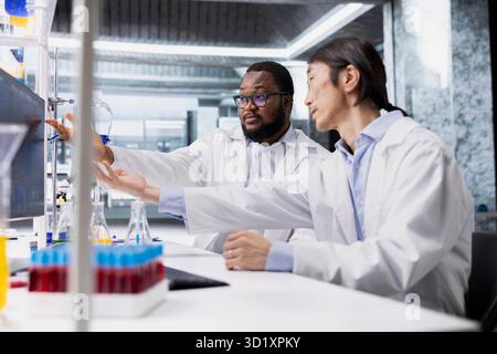 I tecnici di laboratorio multirazziali lavorano insieme al computer per elaborare i dati dei pazienti con DNA per la ricerca clinica. I colleghi di laboratorio multietnici utilizzano il programma PC per eseguire la diagnostica di analisi genetiche di laboratorio Foto Stock