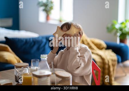 Il ragazzino si ingoiata a giocare con pezzi di pane mentre si siede al tavolo in cucina a casa Foto Stock
