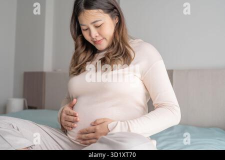 Incinta donna asiatica tiene le mani sulla pancia toccando il suo bambino curando la sua salute bella felice donna incinta tenera umore p Foto Stock
