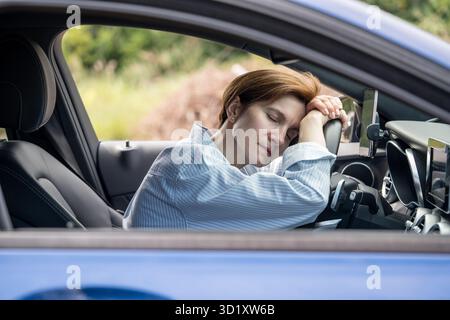 Una donna stanca di mezza età che dorme sul volante è esausta a causa di lunghi viaggi in auto. Foto Stock