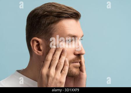 Ritratto di uomo barbuto triste di mezza età che tocca la pelle del viso con ansia per il processo di invecchiamento. Foto Stock