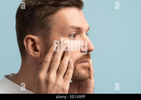 Ritratto di un uomo triste barbuto che tocca la pelle del viso con ansia per il processo di invecchiamento. Foto Stock