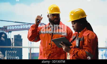 Un esperto ambientale ispeziona le operazioni della piattaforma offshore per individuare l'inquinamento, coordinandosi via radio. I lavoratori dei carri di perforazione valutano la contaminazione dell'oceano, comunicando i risultati con il walkie talkie Foto Stock