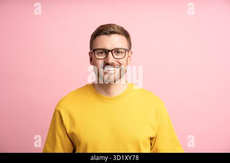Uomo contento sorridente, ritratto su una parete da studio rosa. Un ragazzo istruito e professionale intelligente guarda la fotocamera Foto Stock