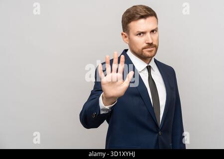 Ritratto di un uomo d'affari serio che mostra il gesto della mano di stop su sfondo grigio. Foto Stock