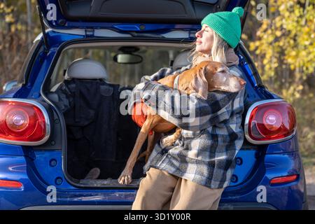 Tenero amante degli animali domestici che si abbraccia con l'amato cane in auto mentre riposa al sole in autunno Foto Stock