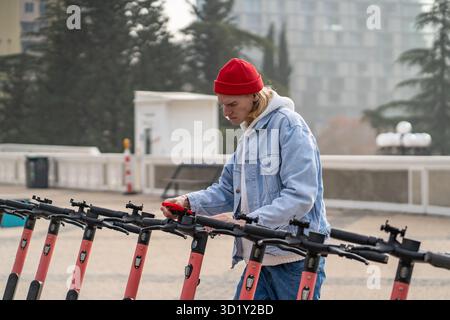Persona concentrata che applica il codice qr sul telefono cellulare per noleggiare uno scooter elettrico in un parcheggio in strada Foto Stock