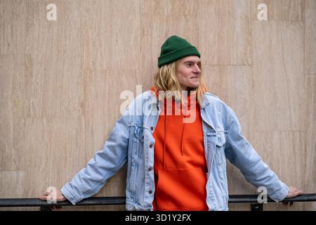 Ritratto cittadino di un ragazzo elegante in un abito colorato alla moda che guarda a distanza, pensando positivo Foto Stock