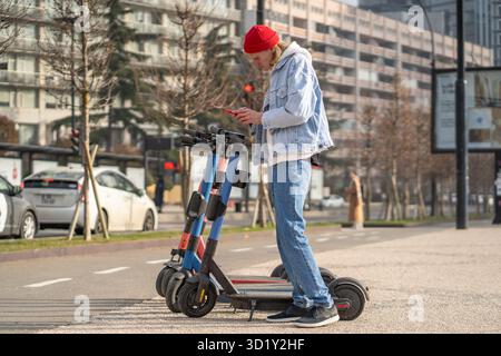 Persona concentrata che applica il codice qr sul telefono cellulare per noleggiare uno scooter elettrico in un parcheggio in strada Foto Stock