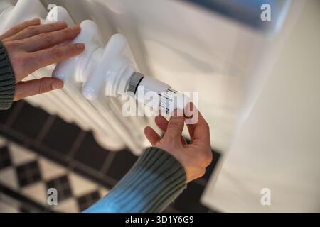 Donna regola il riscaldamento sul radiatore della batteria a casa durante la stagione fredda, con le mani in primo piano. Foto Stock