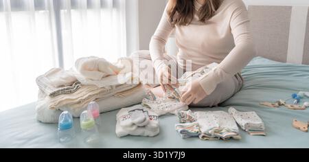 Donna asiatica incinta che si prepara per l'ospedale di maternità preparando e pianificando vestiti per neonato nuovo di gravidanza pac Foto Stock