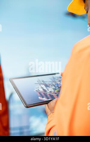 Primo piano di un esperto di carri di perforazione utilizzando il cruscotto dell'app tablet per il rilevamento delle anomalie durante il funzionamento. I dipendenti della piattaforma offshore utilizzano l'interfaccia dell'applicazione per dispositivi per controllare i sistemi in remoto Foto Stock