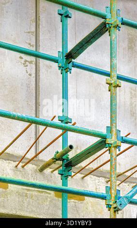 L'impalcatura verde circonda una fila di barre di rinforzo intemprate collegate a una semplice parete di cemento dietro Foto Stock