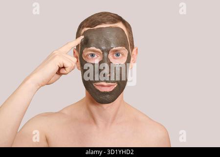 Maschera di argilla nera sulla faccia di Guy. Cosmetology uomo ritratto con fango sano scrub. Maschera ecologica per la natura del carbone. Fango di Dermatologia. Pelle di casa Foto Stock