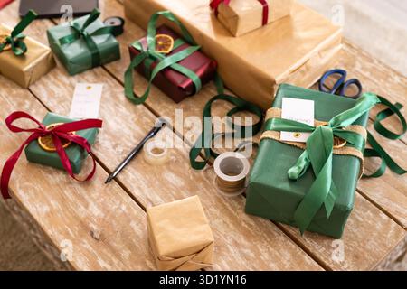Scatola rivestita in verde appoggiata su un tavolo rustico, nastri, etichette, nastro, spago e forbici sparsi Foto Stock