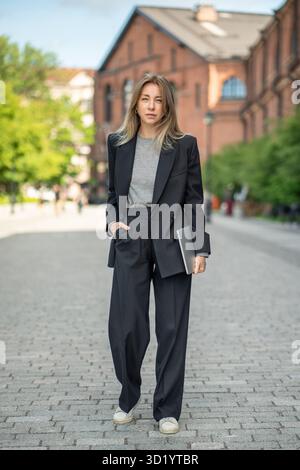 Elegante imprenditrice donna con laptop passeggia per le strade urbane, nomade digitale e freelance Foto Stock