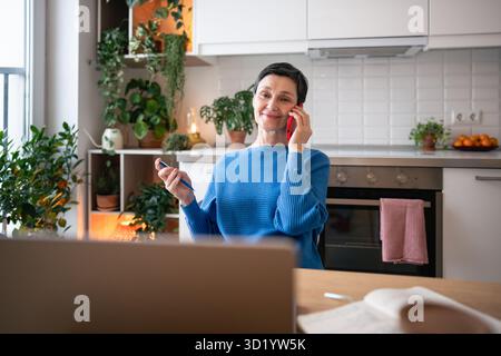 Call center a casa. Donna matura con smartphone che gestisce le attività e l'assistenza clienti in remoto Foto Stock
